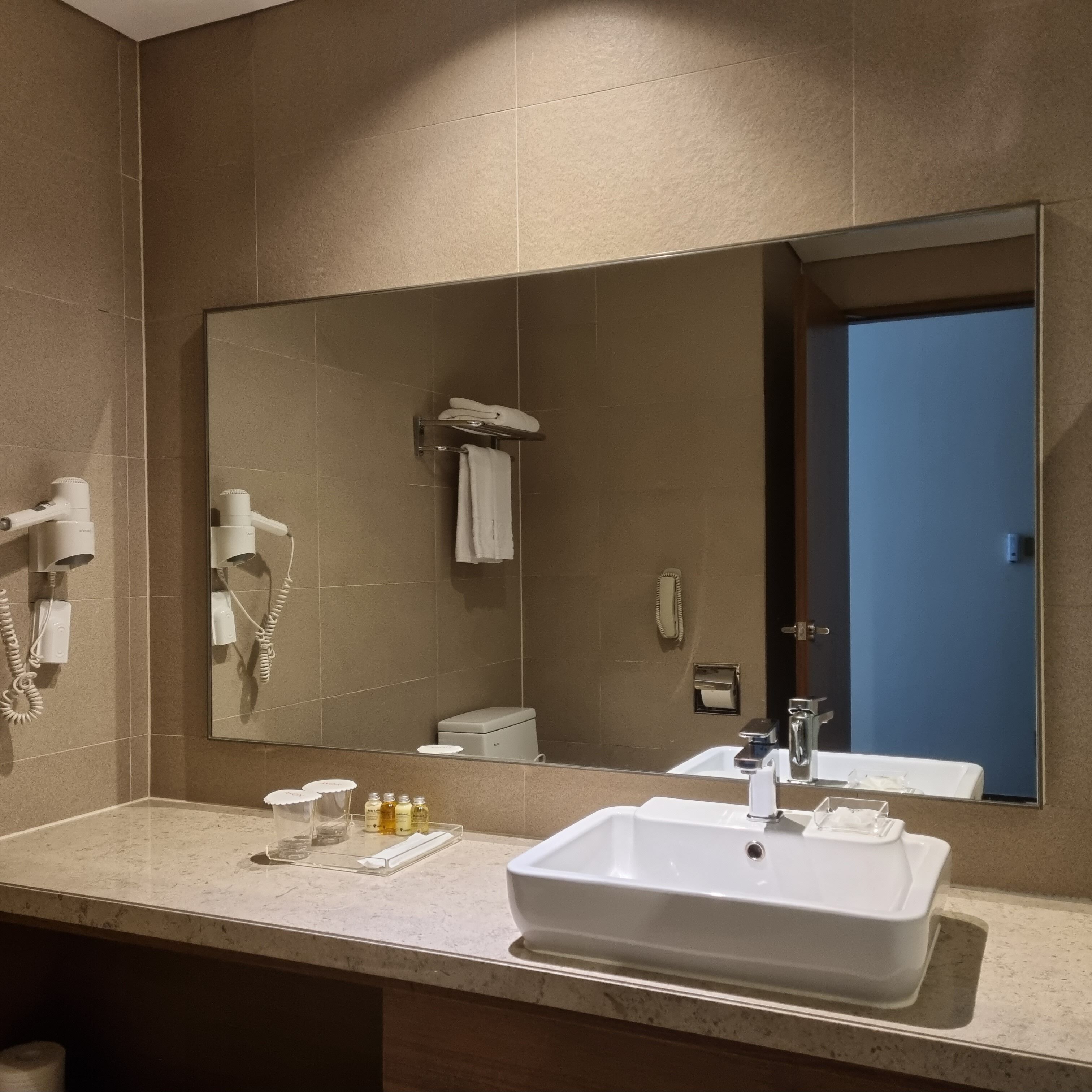 A bathroom with a large mirror, a sink, and a hairdryer mounted on the wall.