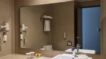 Un baño con un espejo grande, un lavabo y un secador de pelo montado en la pared.