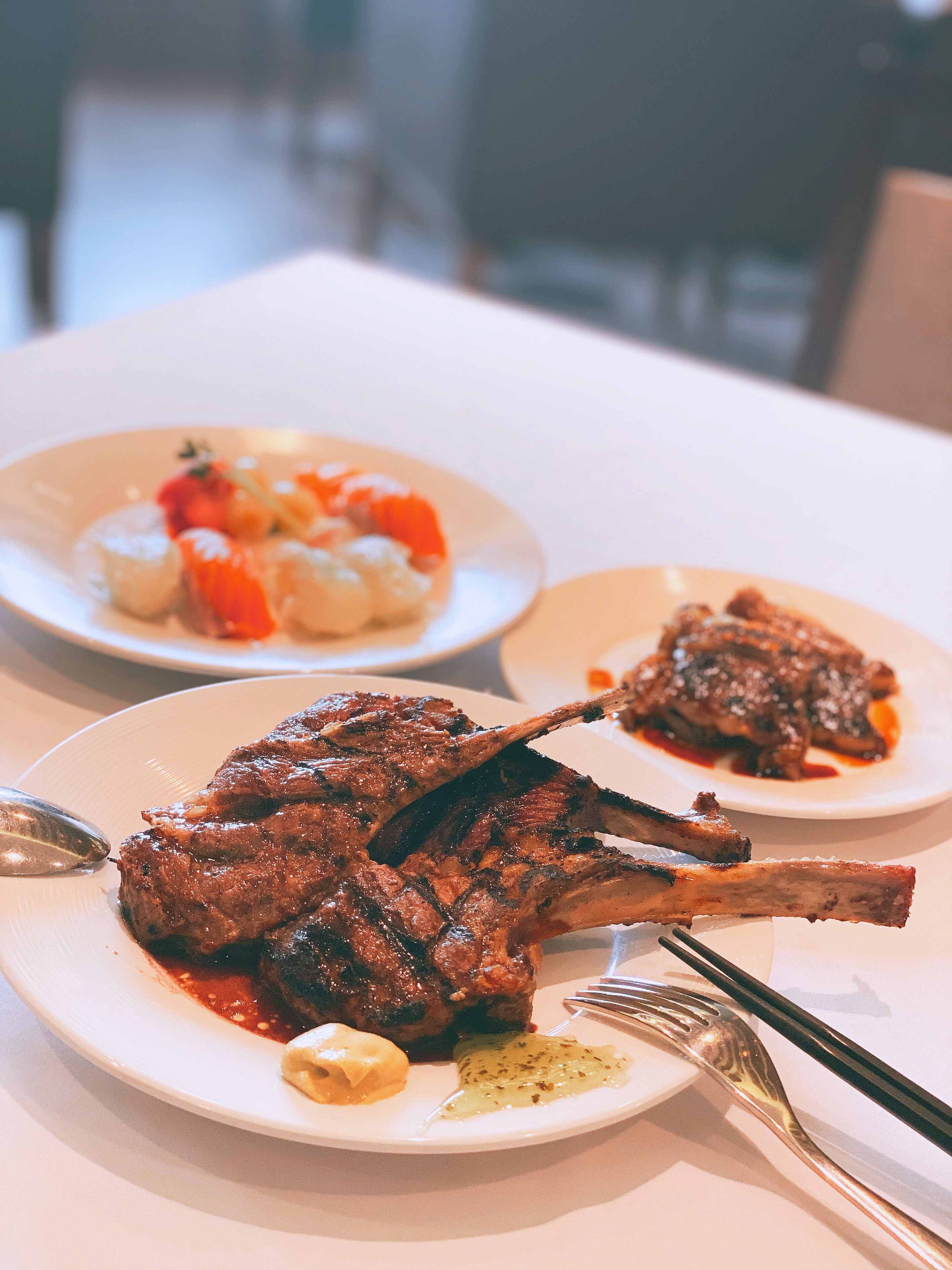A dining table with two plates of food, one with grilled meat and the other with vegetables and a sauce.