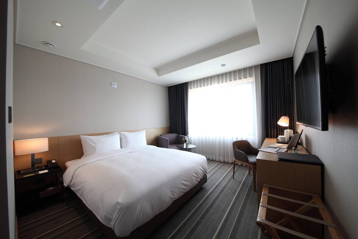 A modern hotel room with a large bed, a desk, a chair, and a TV.