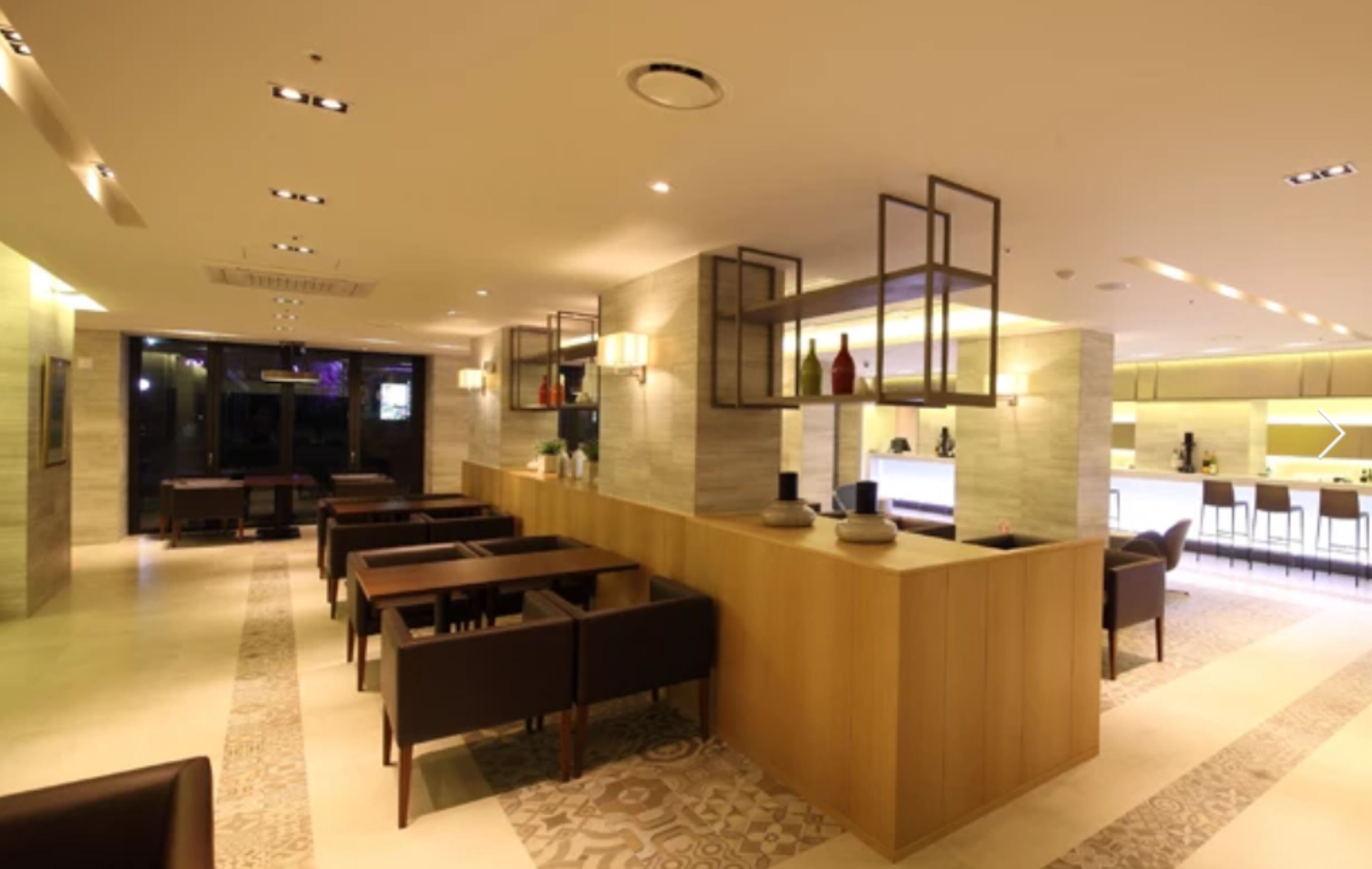 A modern hotel lobby with a reception desk, seating area, and a bar.