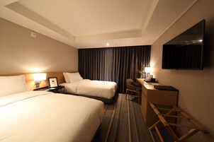 Habitación de hotel con dos camas, un escritorio, una silla, un televisor de pantalla plana y un ventanal con cortinas.