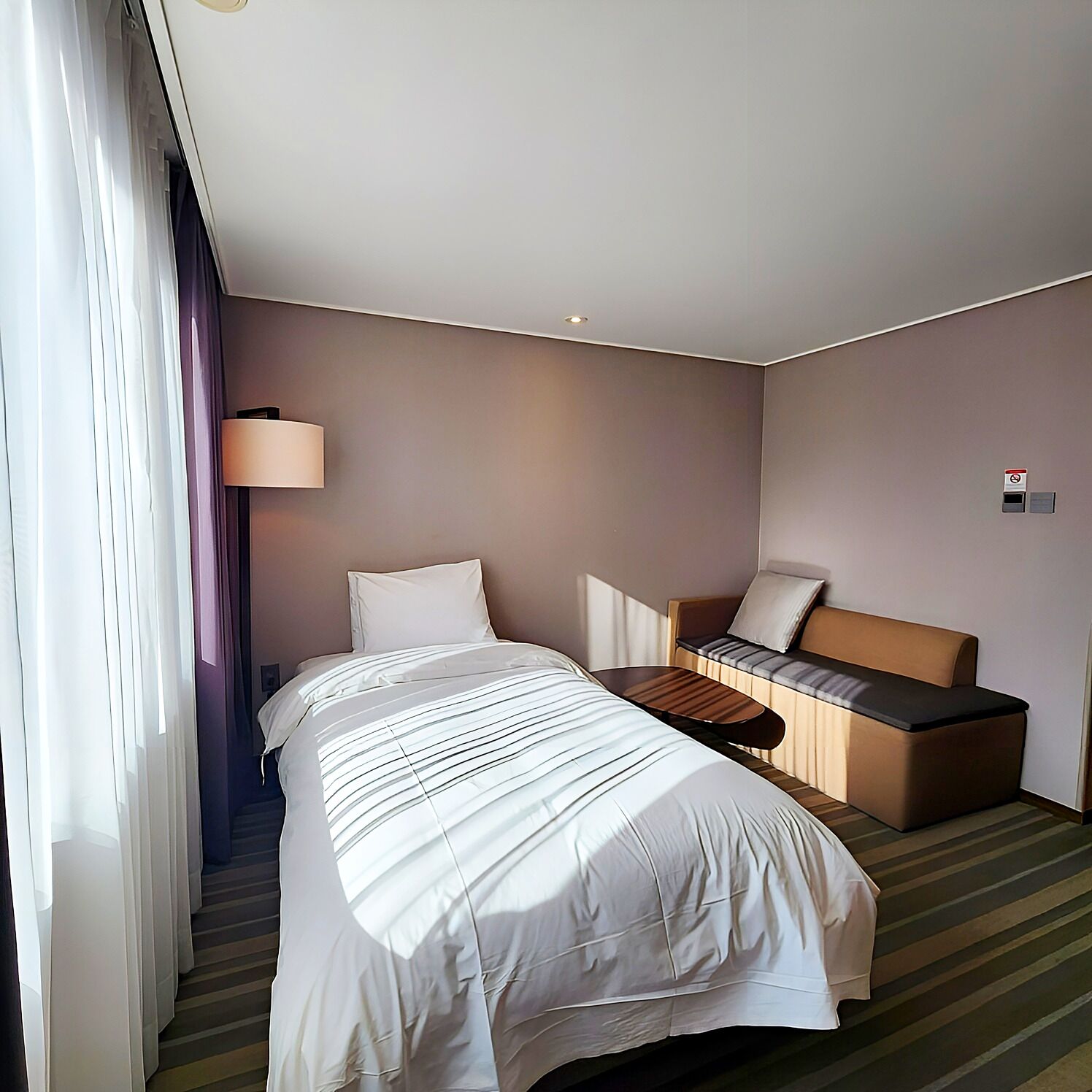A hotel room with a bed, a sofa, a lamp, and a window with curtains.