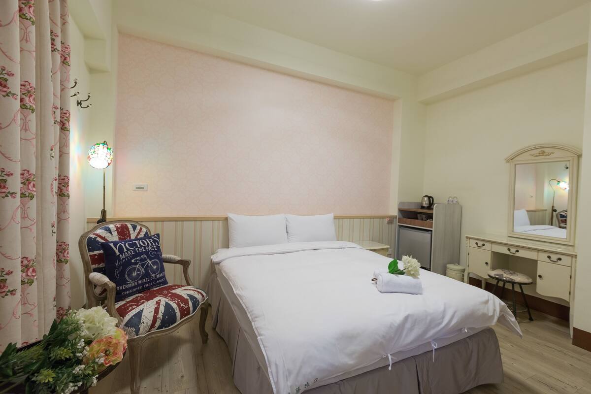 A hotel room with a bed, a chair, a desk, a mirror, and a dresser.