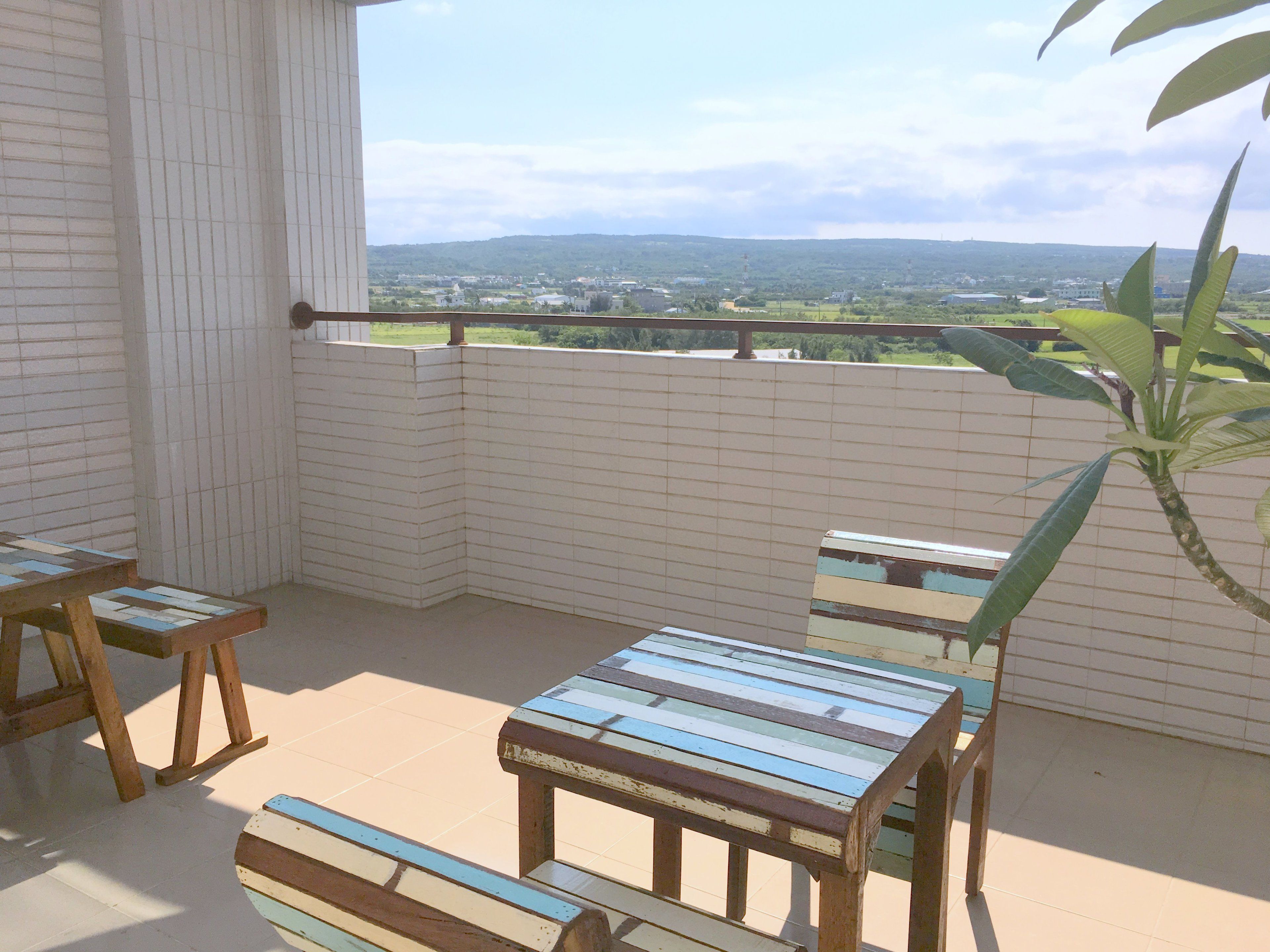 A corner balcony with a view of a distant town and hills.