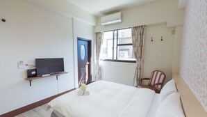 Et hotelværelse med en seng, et fjernsyn på en hylde, et vindue med gardiner, en stol og en aircondition.