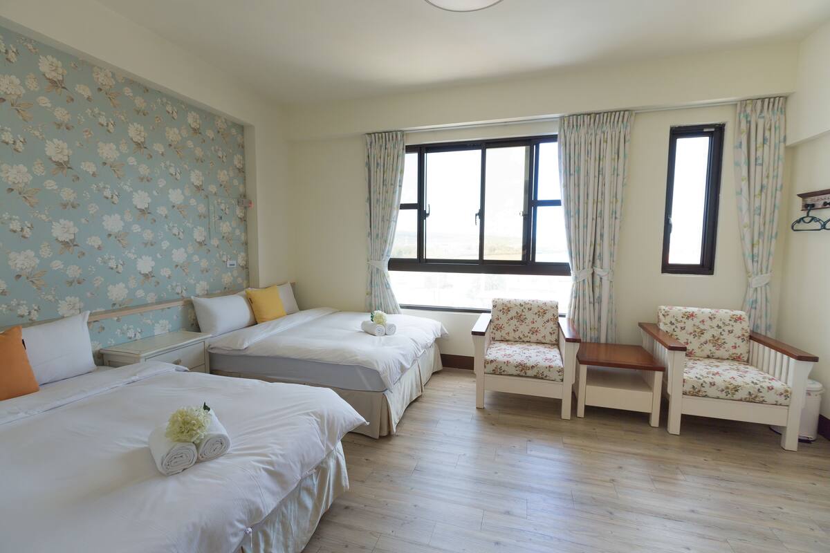 A bedroom with two beds, a chair, a nightstand, and a window with curtains.