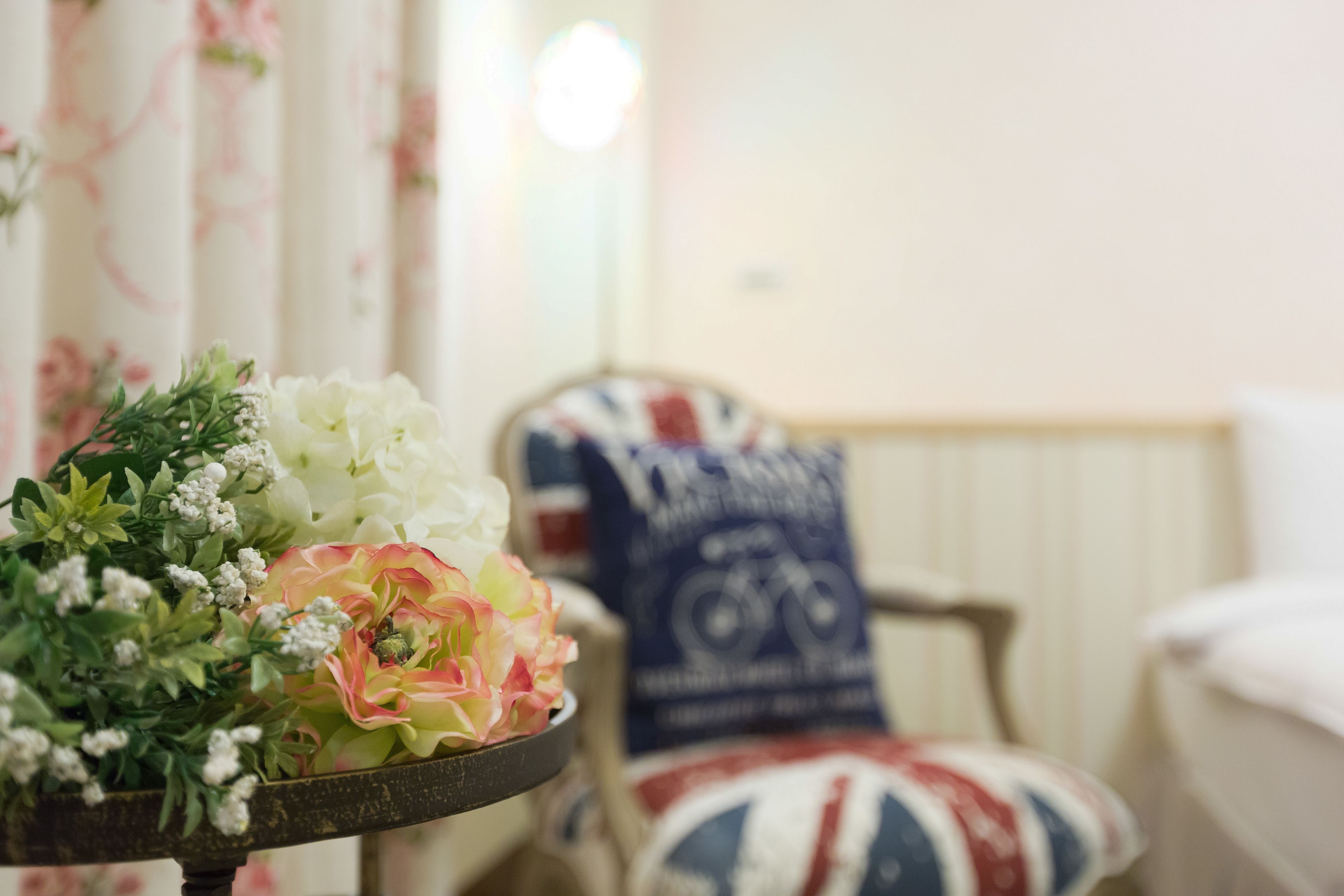 Una habitación con un arreglo floral sobre una mesa, una silla con un cojín con la bandera Union Jack y un radiador al fondo.