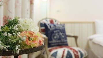 Una habitación con un arreglo floral sobre una mesa, una silla con un cojín con la bandera Union Jack y un radiador al fondo.