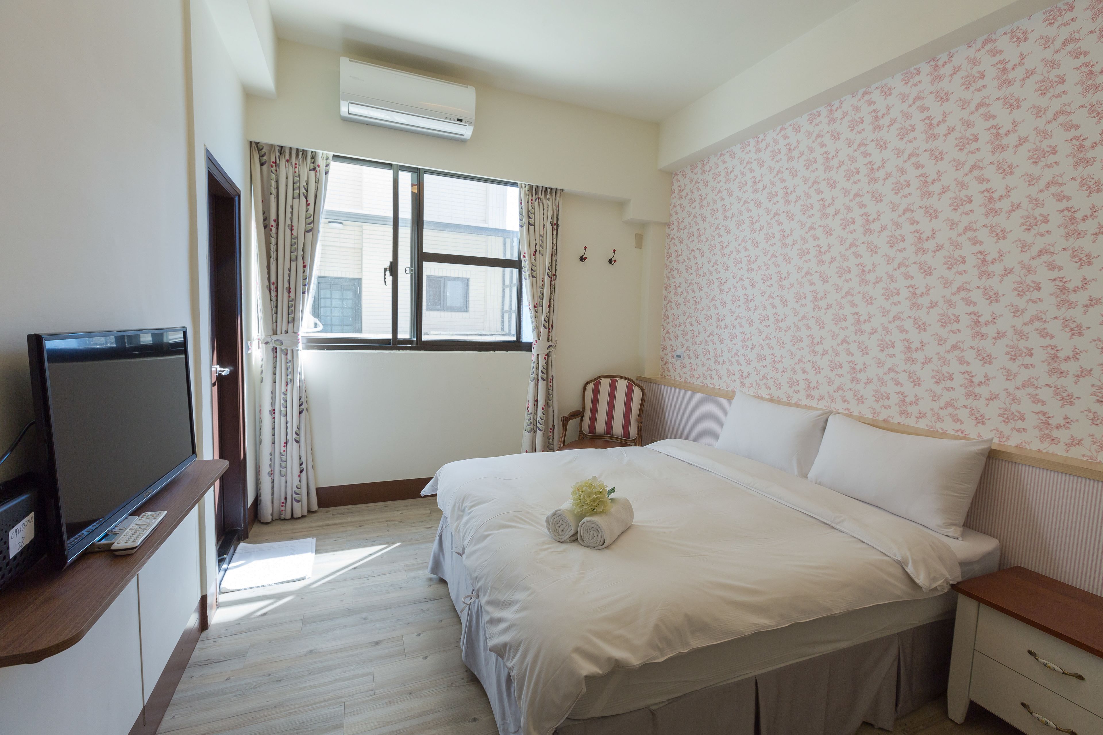 Una habitación de hotel con cama, televisión, silla y ventana con cortinas.