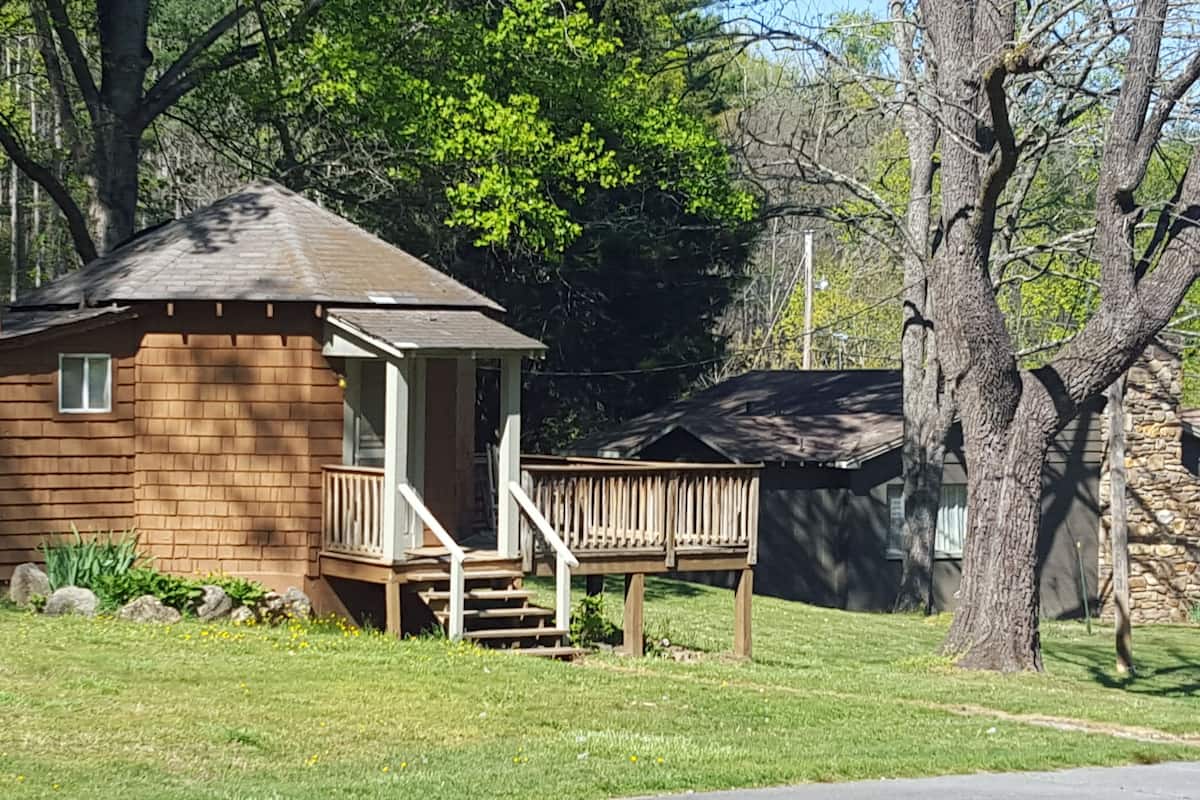 A small wooden cabin with a porch and steps leading up to it, surrounded by trees and grass.