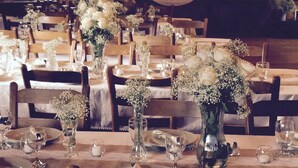 A dining area with wooden tables set for a meal, each with a vase of flowers and glassware.