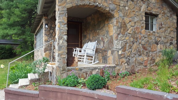 A stone house with a porch, a rocking chair, and a small garden.