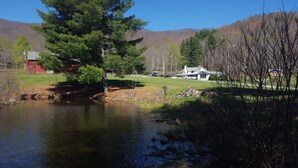 A lakeside property with a large house, a red barn, and a forested backdrop.