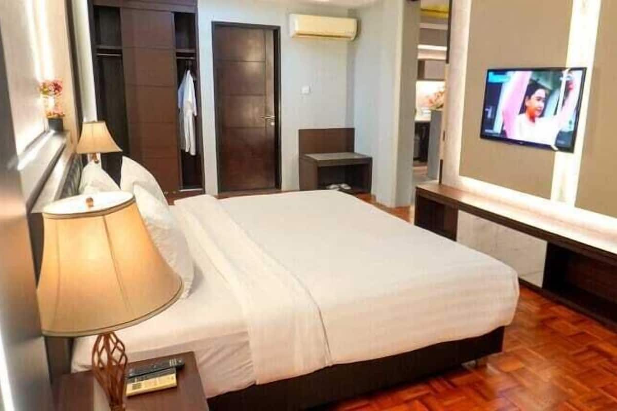 A hotel room with a bed, a TV mounted on the wall, a bedside table with a lamp, and a wardrobe.