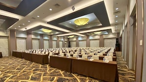 Un salón de conferencias con mesas, sillas dispuestas en filas y una alfombra estampada.