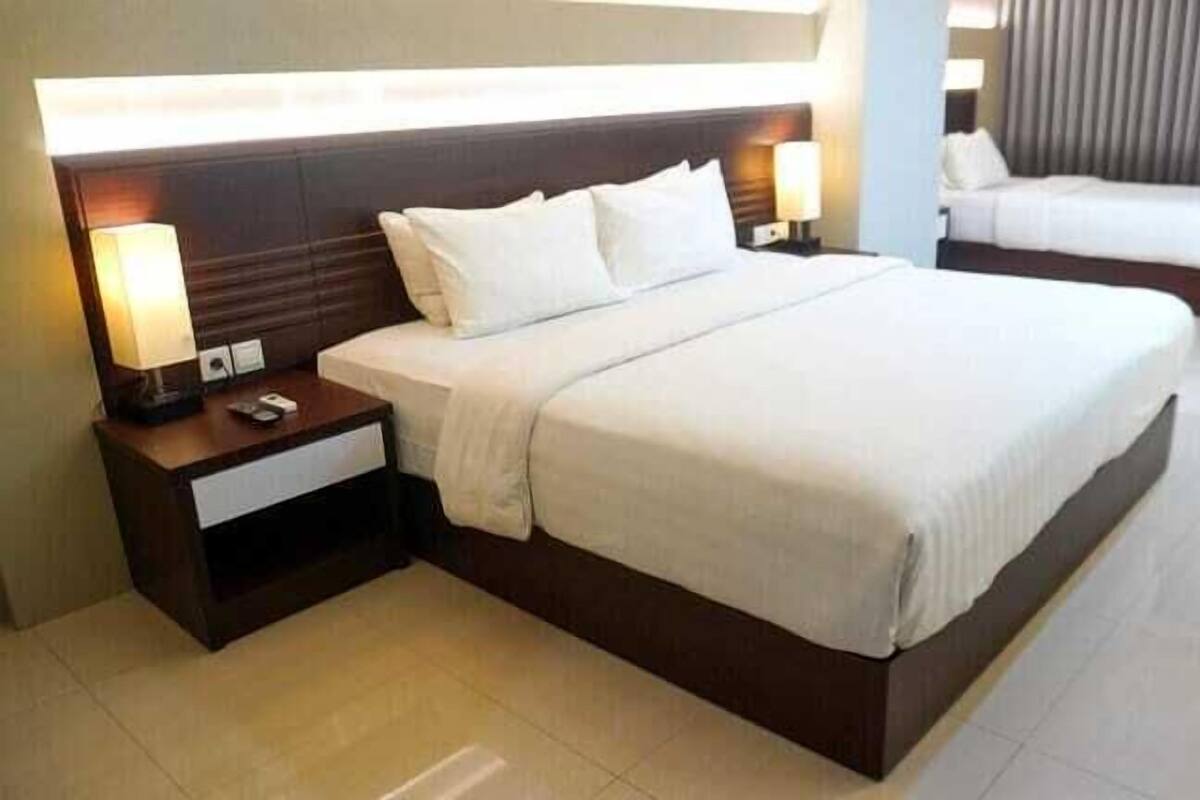 A hotel room with a large bed, two bedside tables with lamps, and a separate bed in the background.