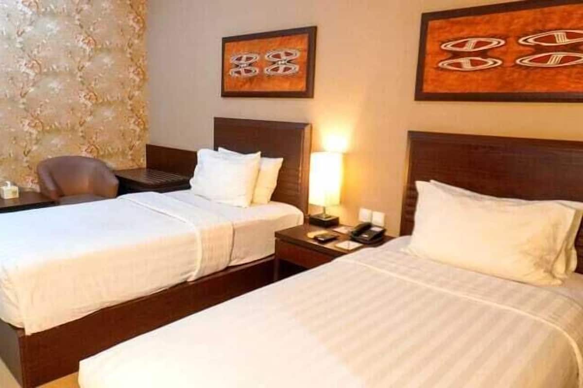 A hotel room with two beds, a desk, a chair, and artwork on the walls.