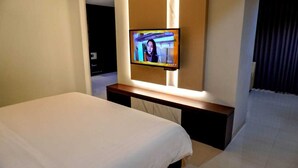 Una habitación de hotel con una cama, un televisor montado en la pared y un escritorio pequeño.