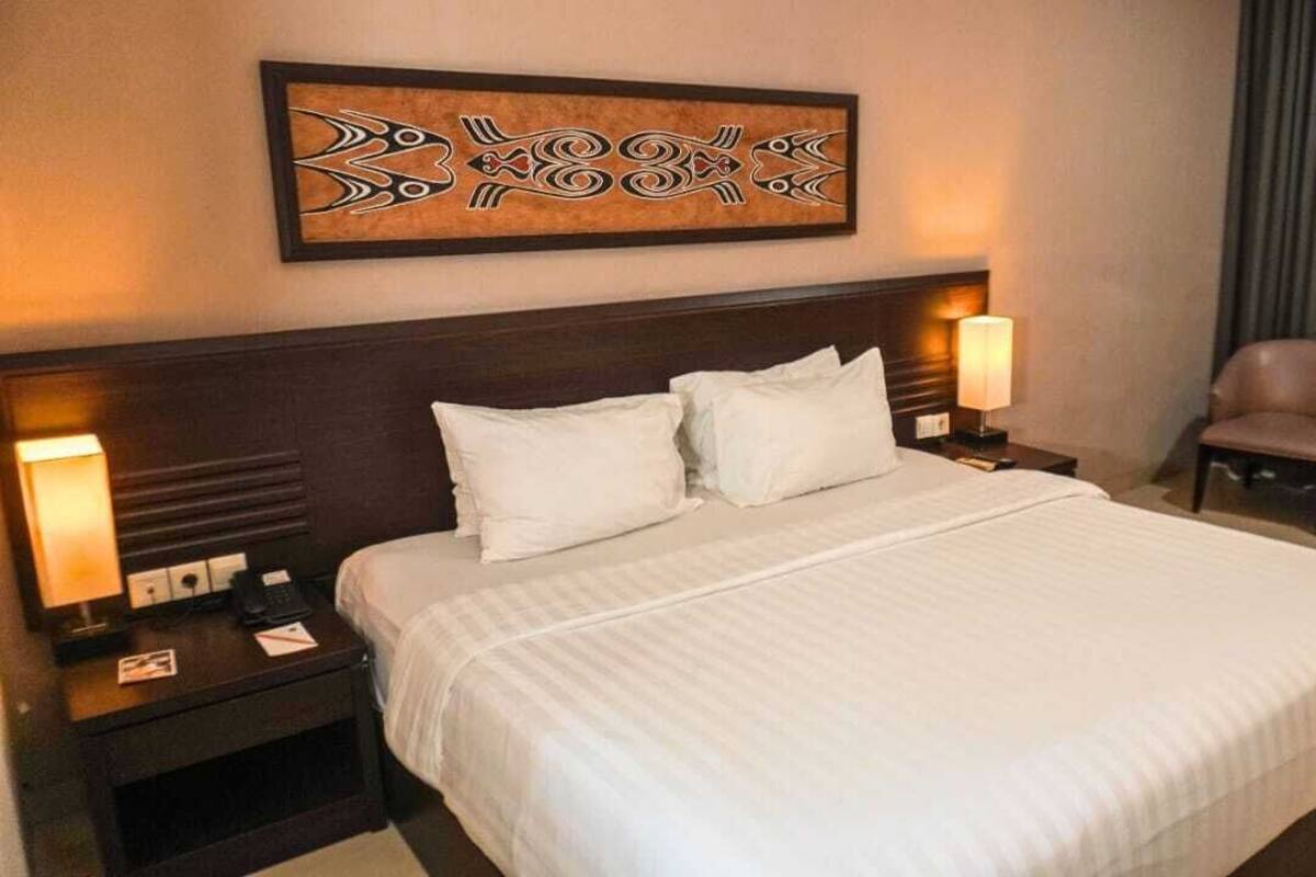 A hotel room with a large bed, two bedside tables with lamps, a headboard, and a framed artwork above the bed.