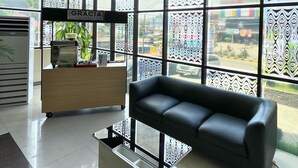 Una habitación amplia con ventanas grandes, un sofá de cuero negro, un escritorio de madera y una cafetera.