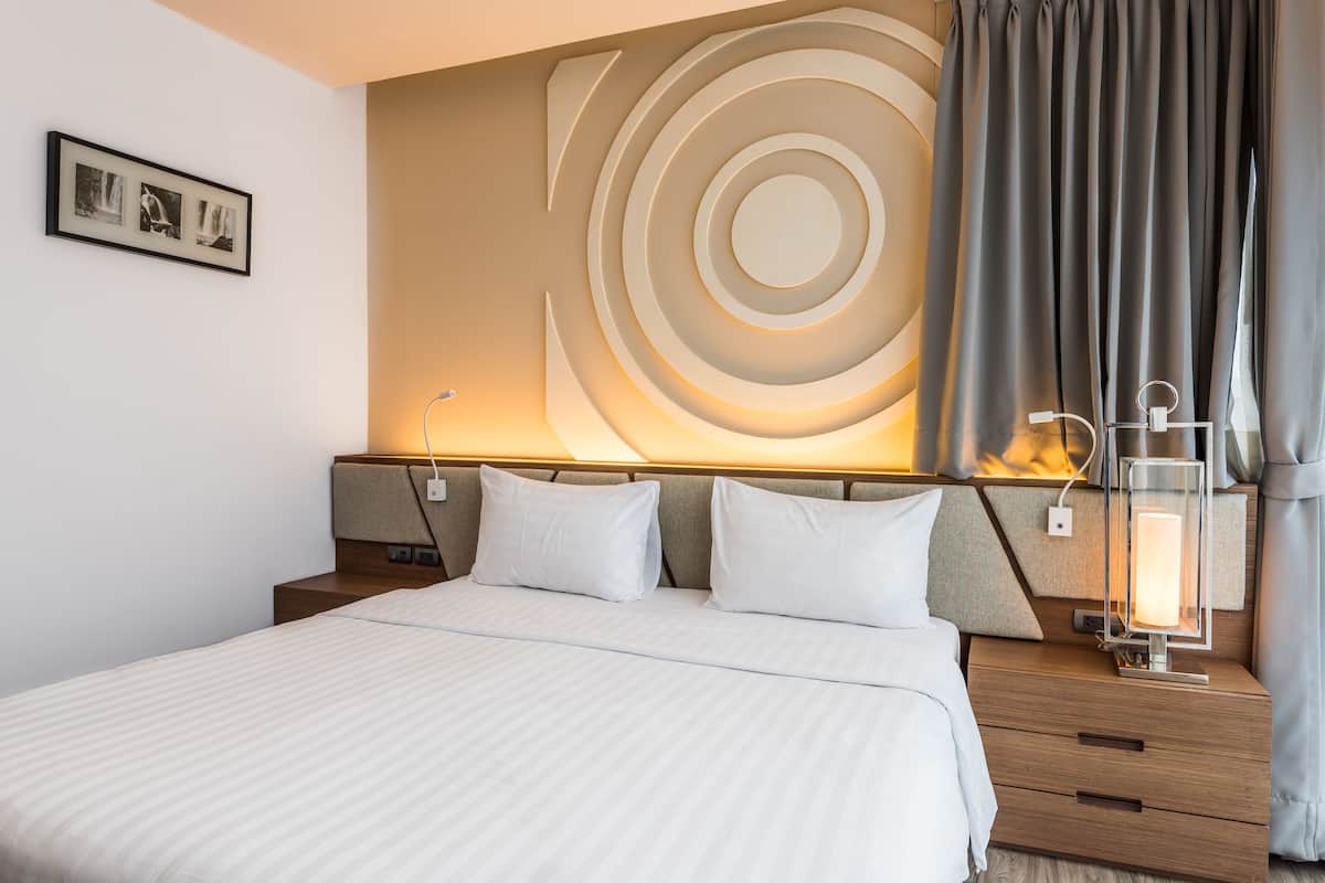A neatly made bed with a headboard, a bedside table with a lamp, and a wall with a circular design.
