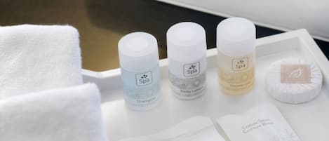 A bathroom with a white sink, a towel, and three bottles of spa products on a tray.
