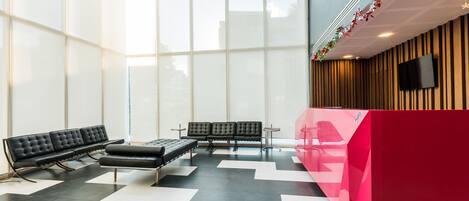 A modern waiting area with black leather benches, a red reception desk, and a large window providing natural light.