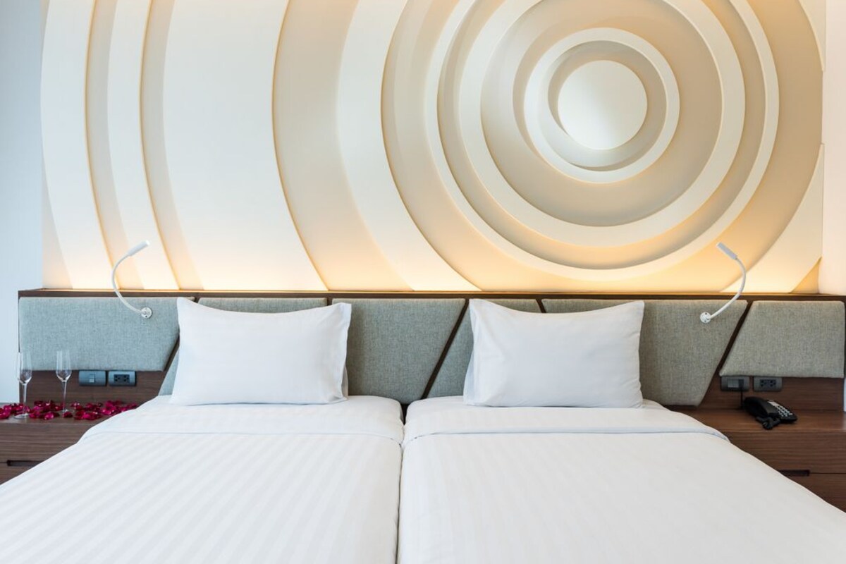 Habitación de hotel con cama doble, dos mesitas de noche, lámpara de pared y un diseño decorativo en la pared.