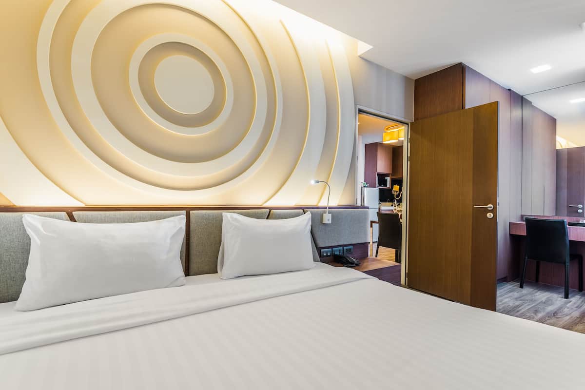 A modern hotel room with a large bed, a wooden door, and a desk with a chair.