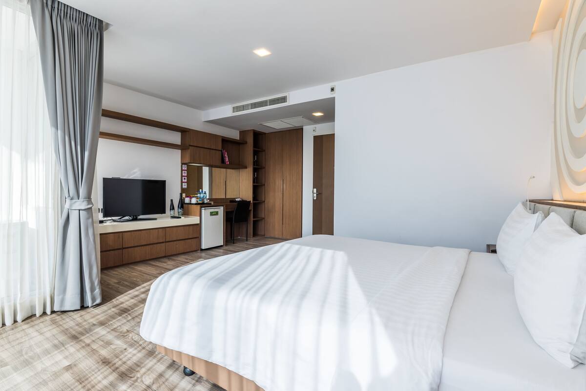 A hotel room with a large bed, a desk with a television, a minibar, and a wardrobe.