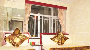 A hotel room with two beds, each with a decorative pillow, a window with curtains, and a small table with a vase and cups. - New Reliance Inn (Kowloon)