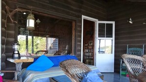 Interior rústico de una cabaña con una cama, muebles de mimbre, una mesa con lámpara y una estantería.