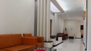 A modern hotel lobby with a long reception desk, a sofa, and a coffee table. - Pondok Asri Family Guest House (Surabaya)