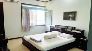 A bedroom with a bed, a nightstand, a dresser, a window with curtains, and a painting on the wall. - Pondok Asri Family Guest House (Surabaya)
