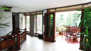 A spacious room with a wooden staircase, large windows, and a balcony with chairs. - Pondok Asri Family Guest House (Surabaya)