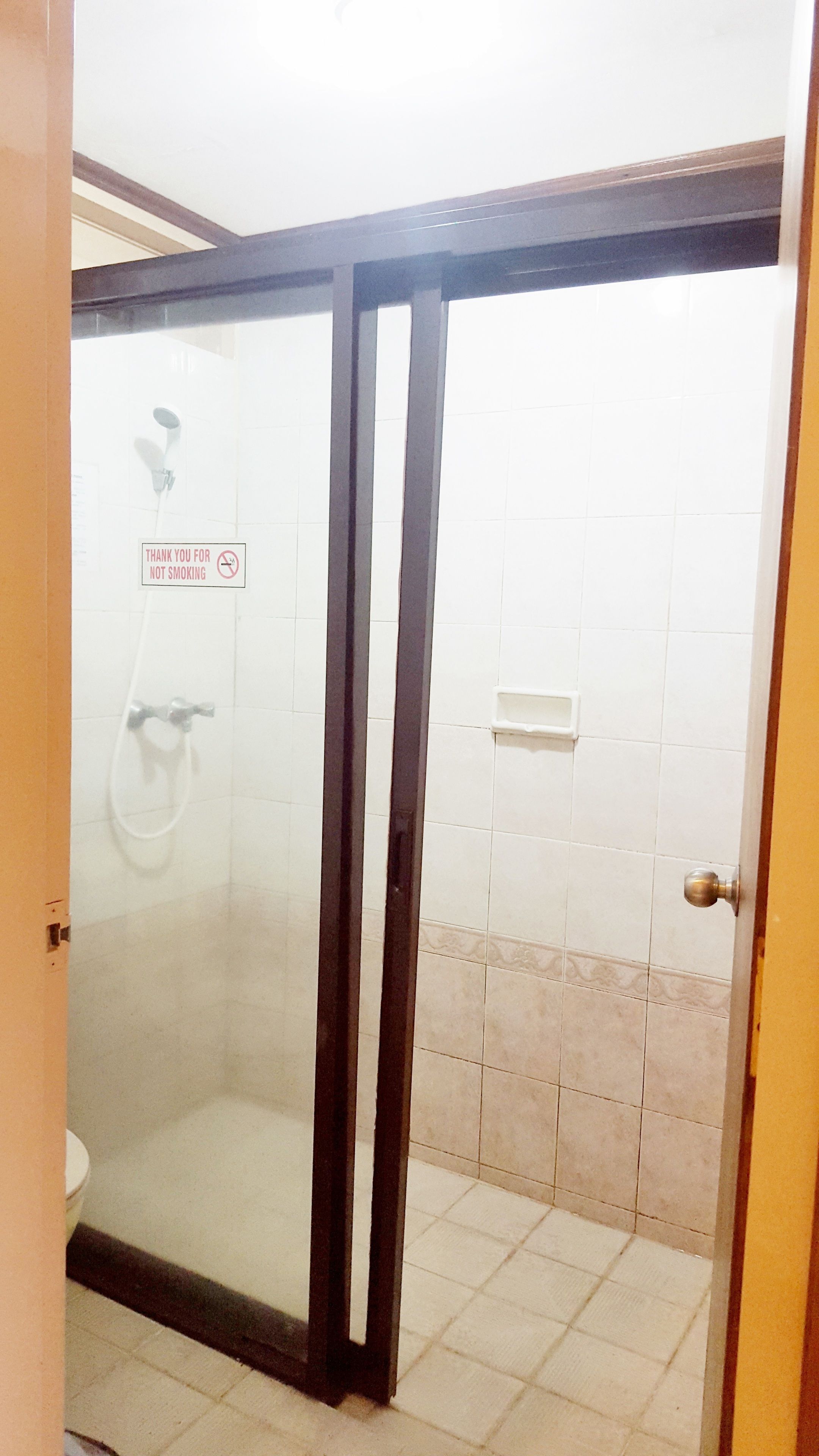 Un bagno con box doccia in vetro, pareti piastrellate di bianco e un cartello con la scritta ‘Grazie per non fumare’.