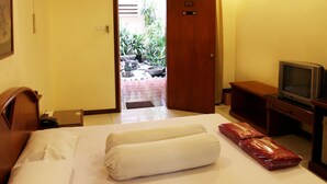 A hotel room with a bed, a television, a desk, and a door leading to a balcony with plants. - Pondok Asri Family Guest House (Surabaya)