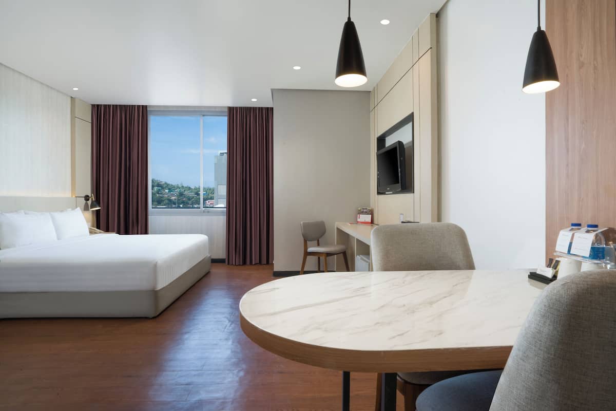 Ein Hotelzimmer mit Bett, Schreibtisch, Stuhl, Fernseher und einem Fenster mit Vorhängen.