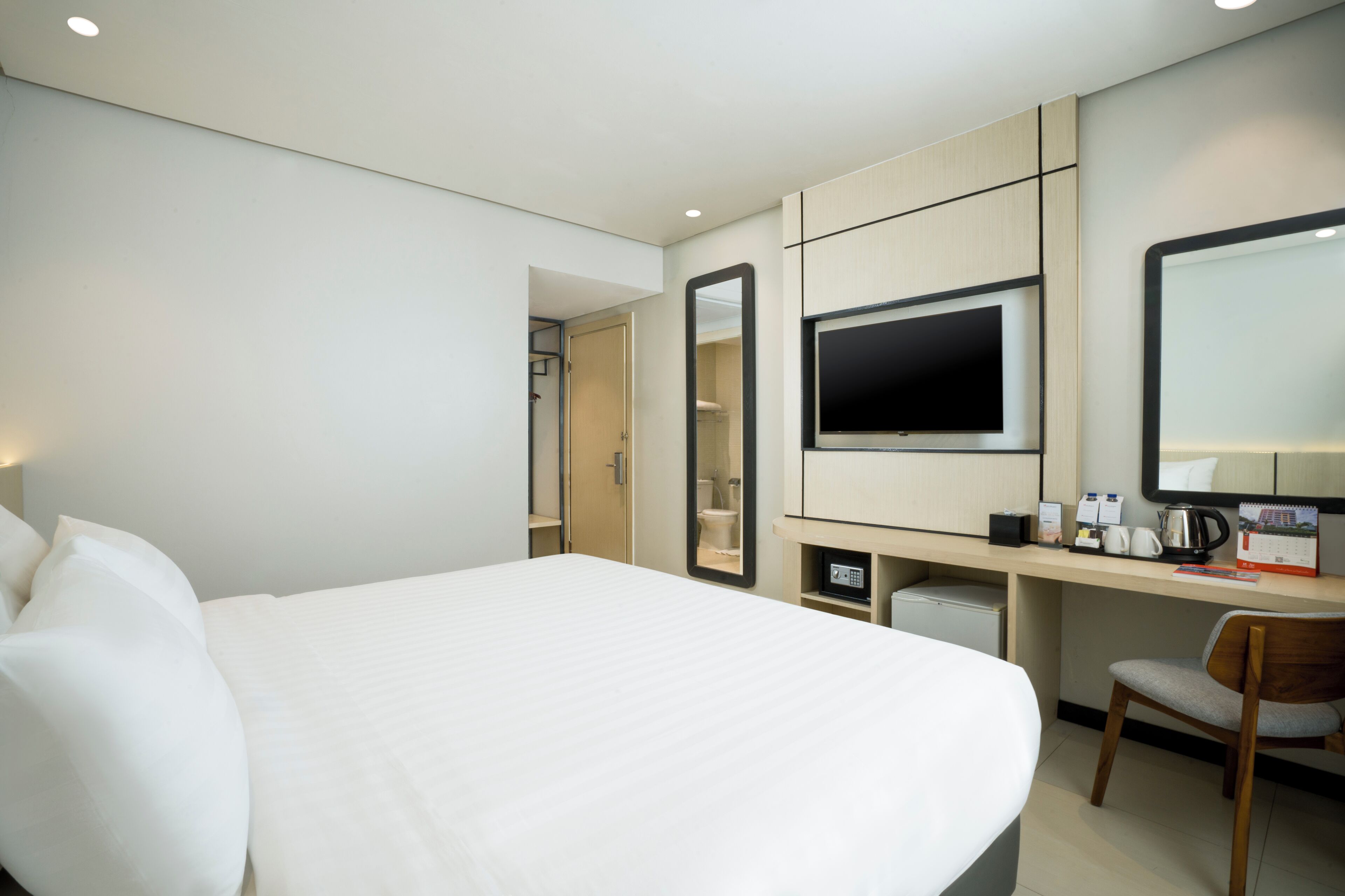 A hotel room with a large bed, a desk with a computer, a chair, a TV, and a mirror.