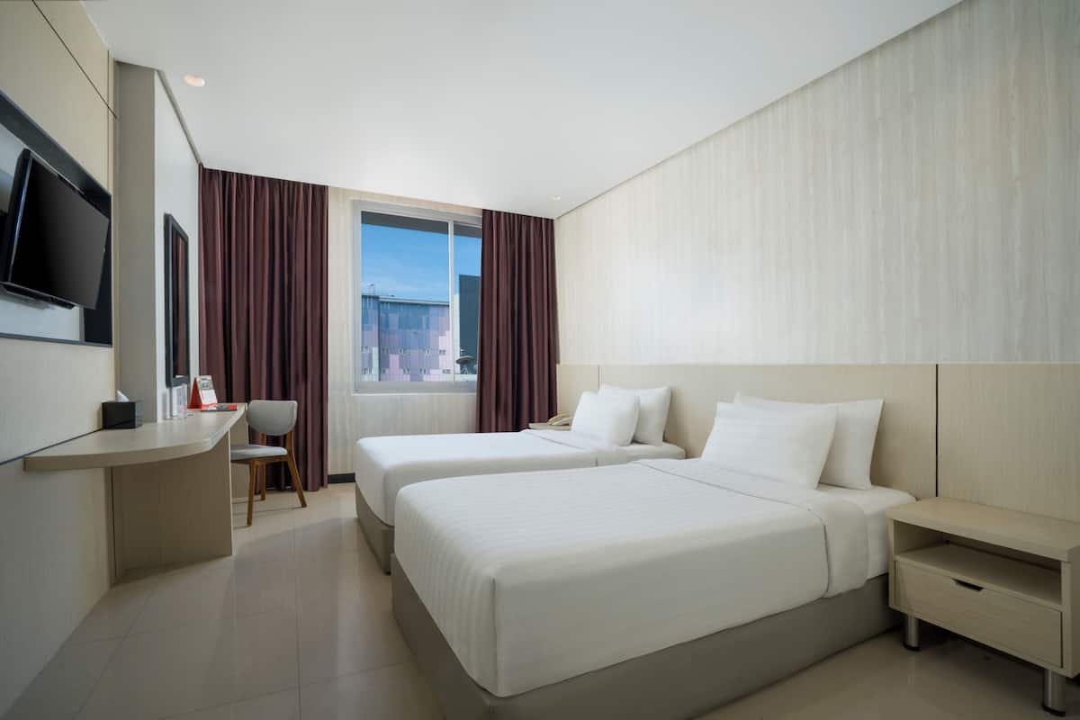 Ein Hotelzimmer mit zwei Betten, einem Schreibtisch, einem Stuhl, einem Fernseher und einem Fenster mit Vorhängen.