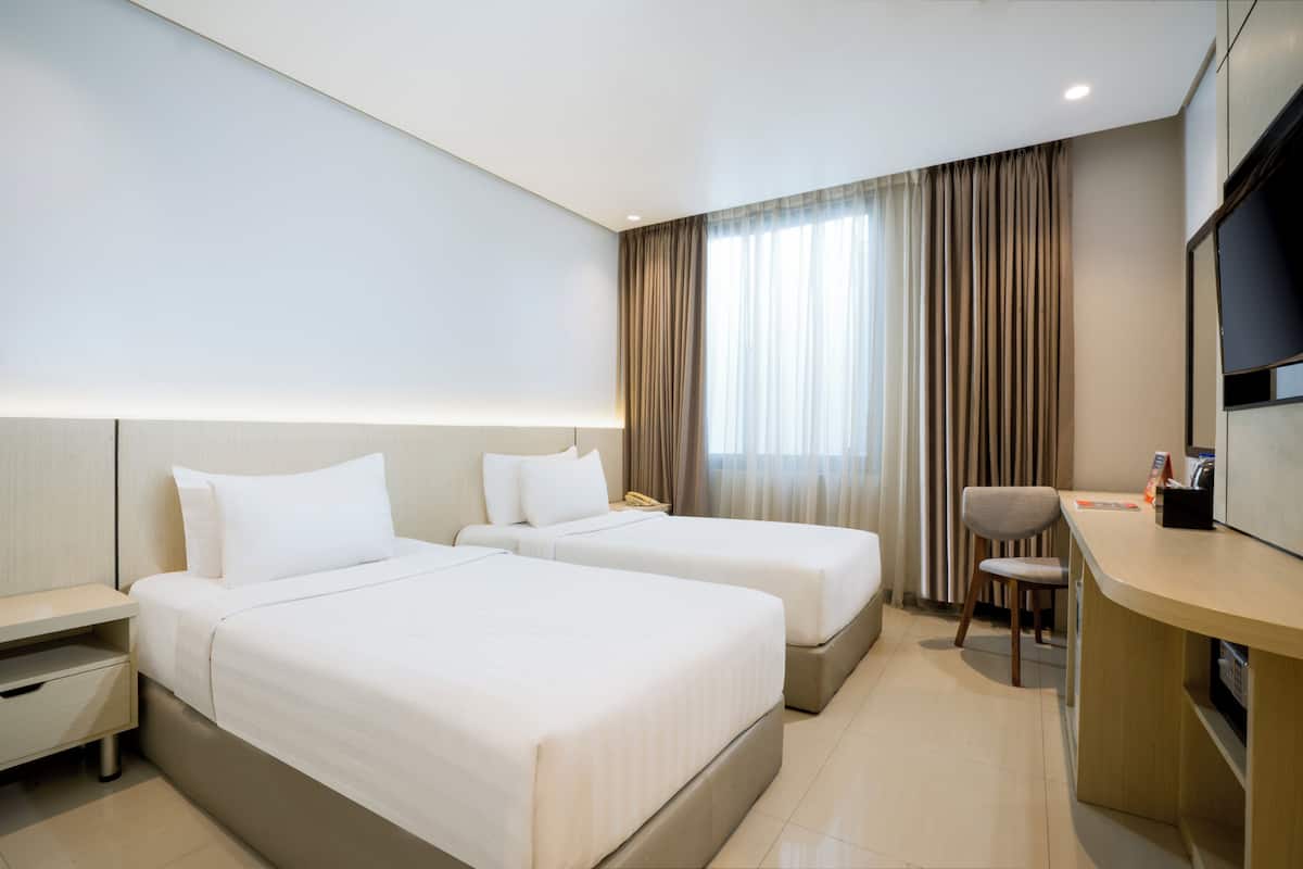 Ein Hotelzimmer mit zwei Betten, einem Schreibtisch, einem Sessel, einem Fernseher und einem Fenster mit Vorhängen.