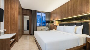 Ein Hotelzimmer mit einem großen Bett, einem Schreibtisch, einem Sessel und Blick auf die Stadt durch das Fenster.