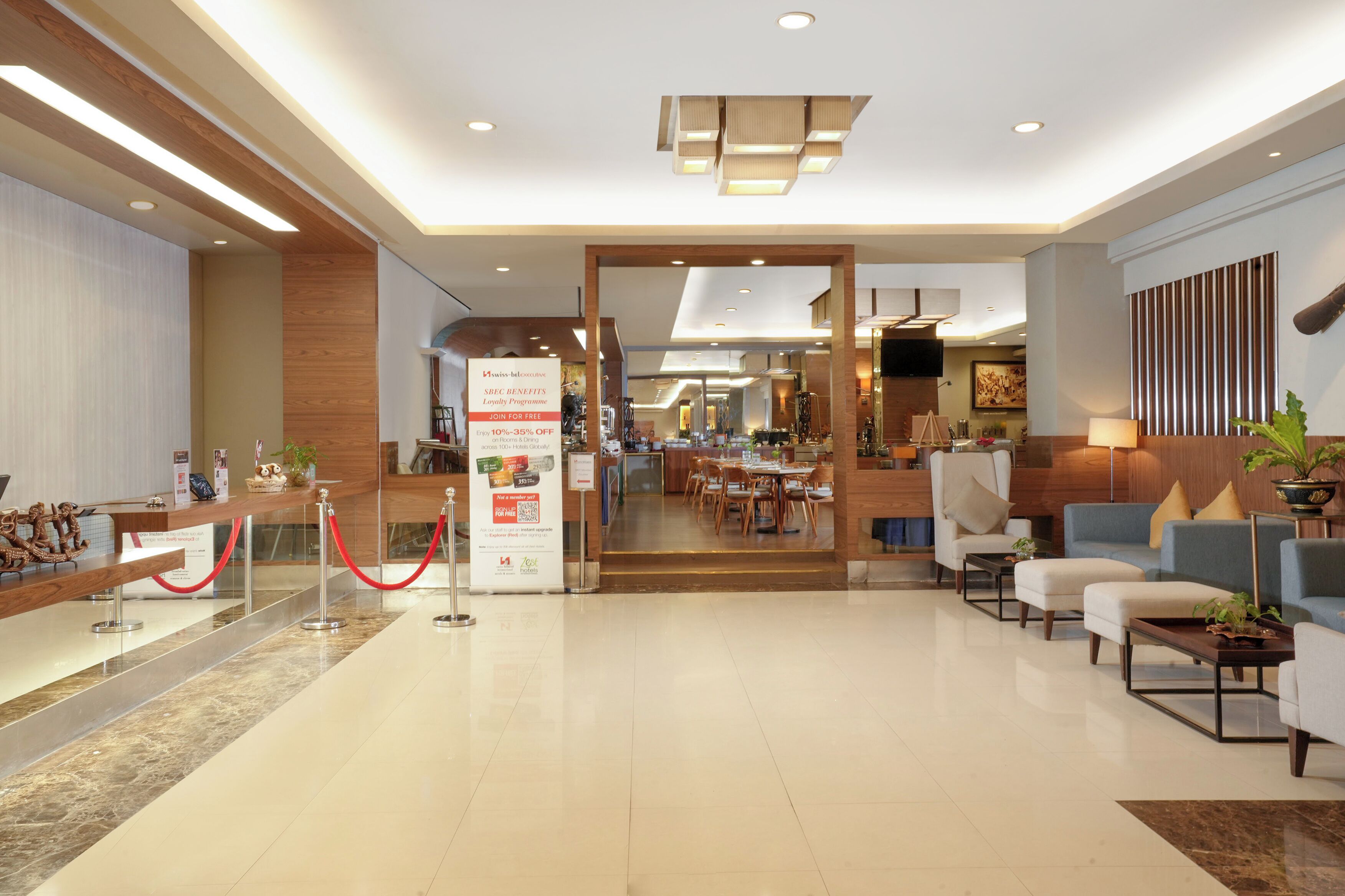 A modern hotel lobby with a reception desk, seating area, and a dining space.