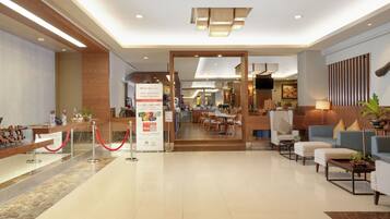 A modern hotel lobby with a reception desk, seating area, and a dining space.