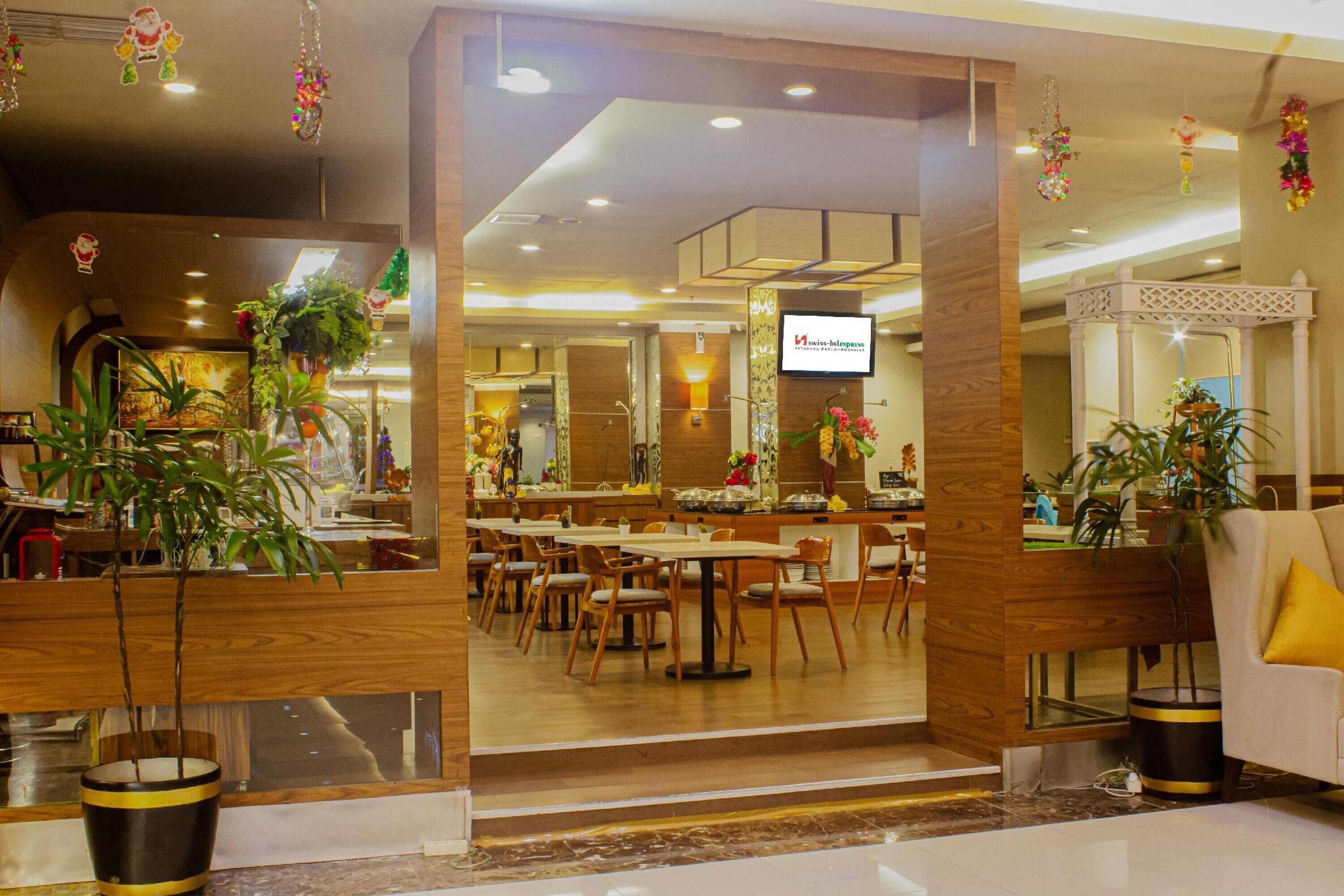 A modern hotel lobby with wooden accents, a TV screen, and several potted plants.