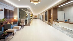 Eine moderne Hotelhalle mit Empfangstresen, Sitzgelegenheiten und einem Gang zu den Zimmern.