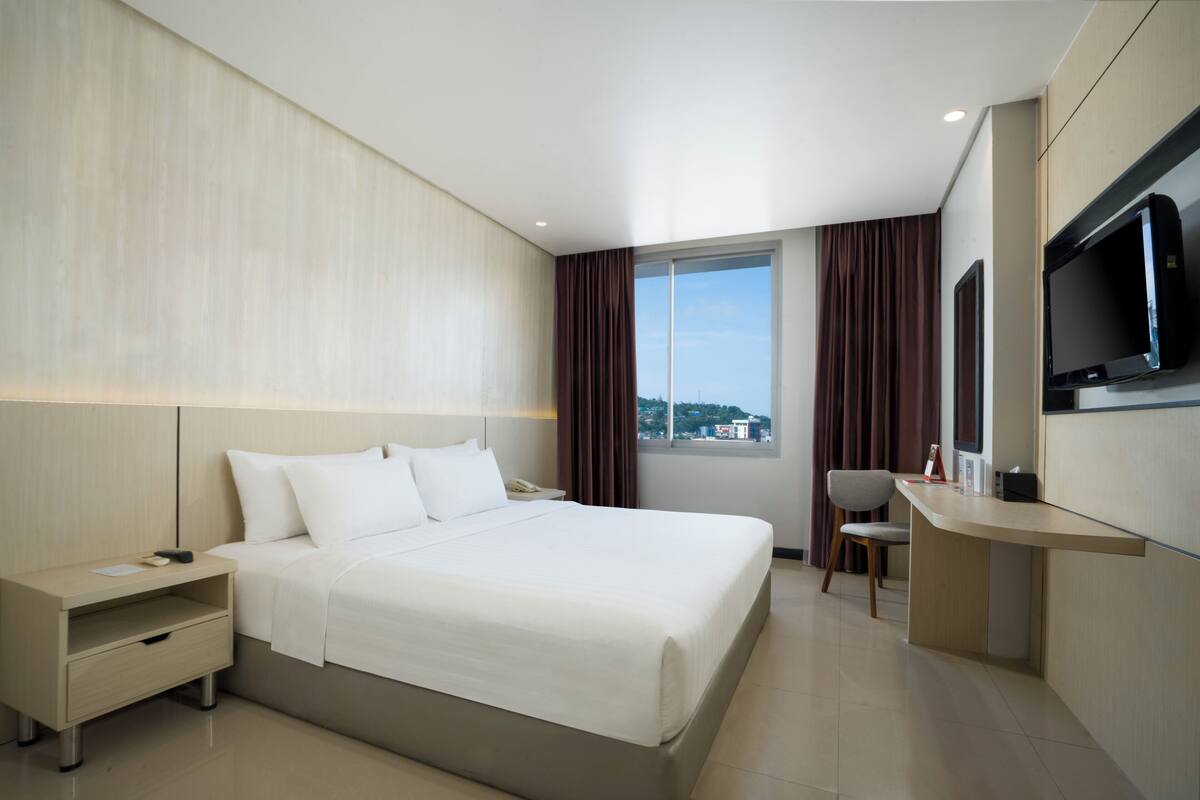 Ein modernes Hotelzimmer mit einem großen Bett, einem Schreibtisch und einem Fernseher.