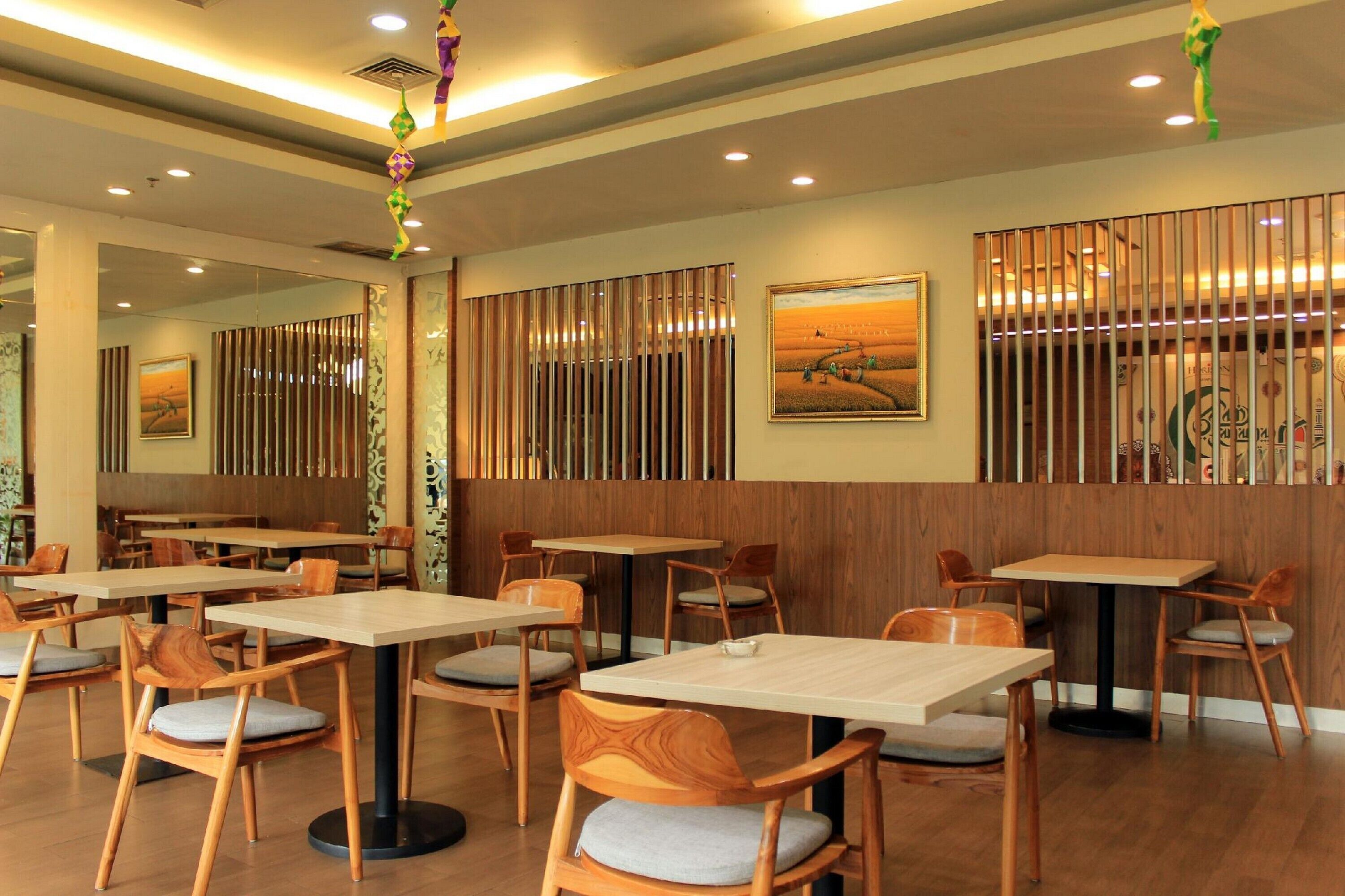 Un interior de restaurante con mesas y sillas de madera, un adorno colgante y un cuadro en la pared.