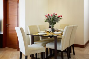 A dining area with a wooden table, four chairs, a vase with flowers, and a bottle of wine.